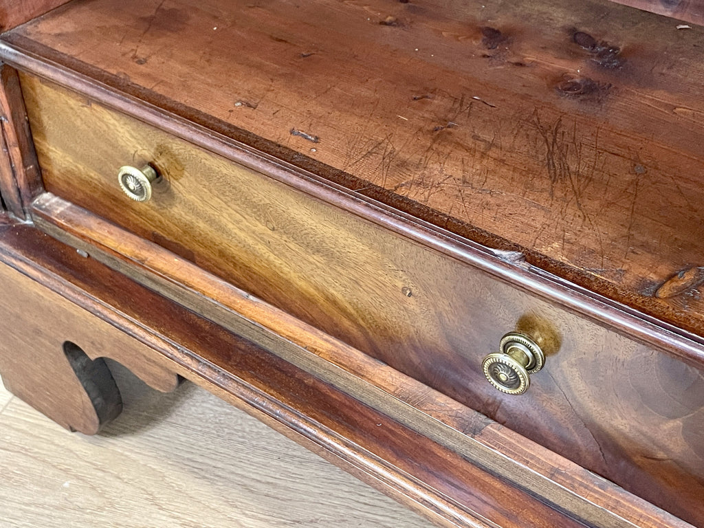 Close-up of a wooden drawer with brass handles on a light wood floor.