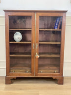 Wooden display cabinet with glass doors against a white wall.