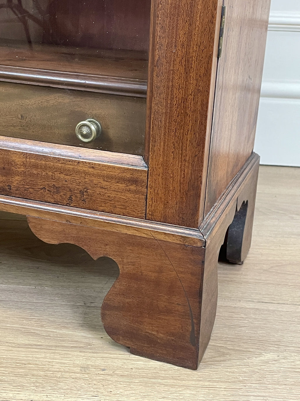 Wooden cabinet with glass door and metal handle on a wooden floor.
