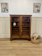 Wooden bookshelf with glass doors in a room with wainscoting and framed pictures.
