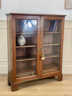 Wooden display cabinet with glass doors in a room with white paneled walls.