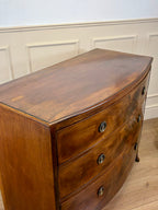 Wooden dresser with curved top against a white paneled wall.