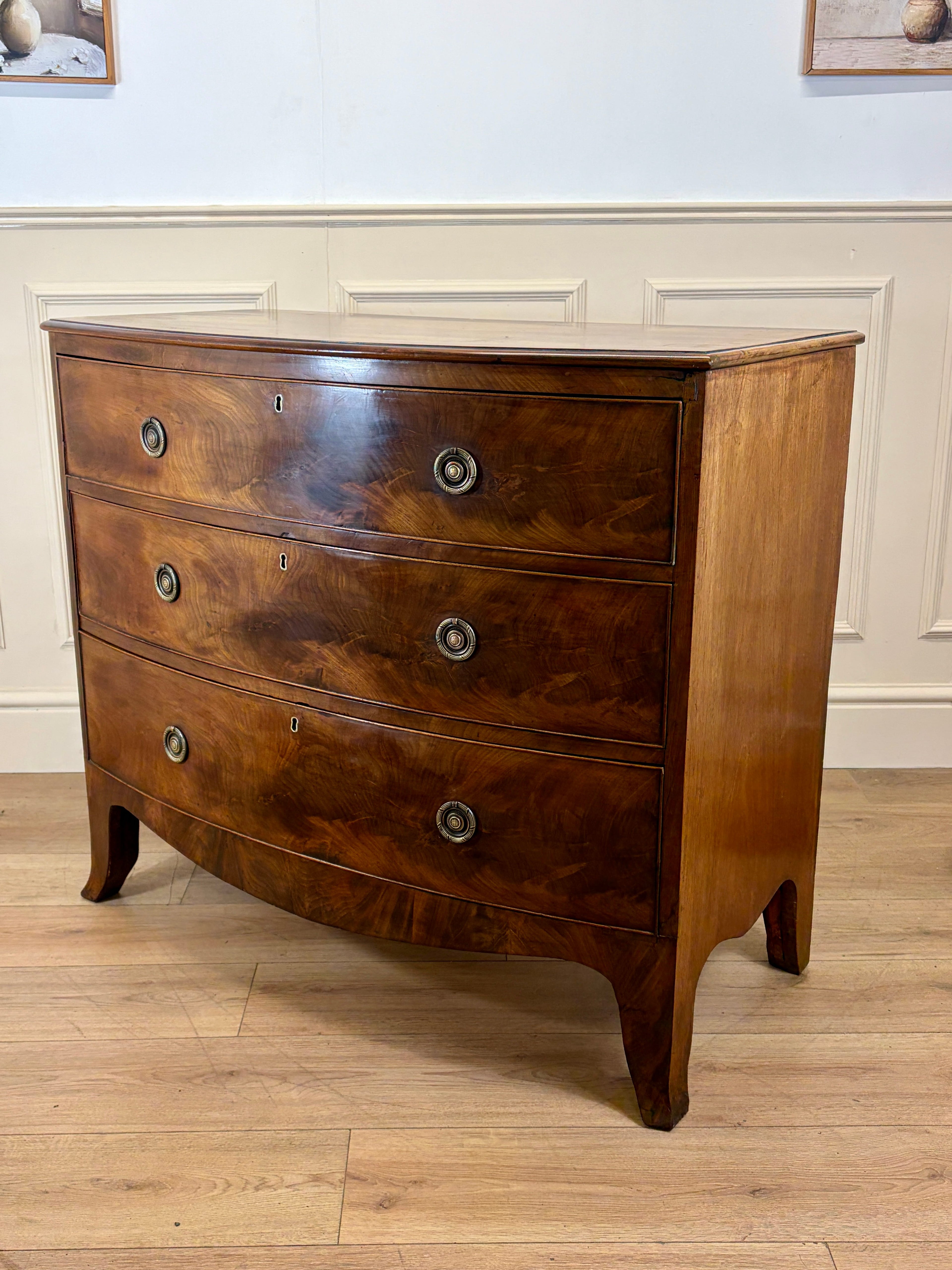 Wooden dresser with curved design on a wooden floor against a white wall.