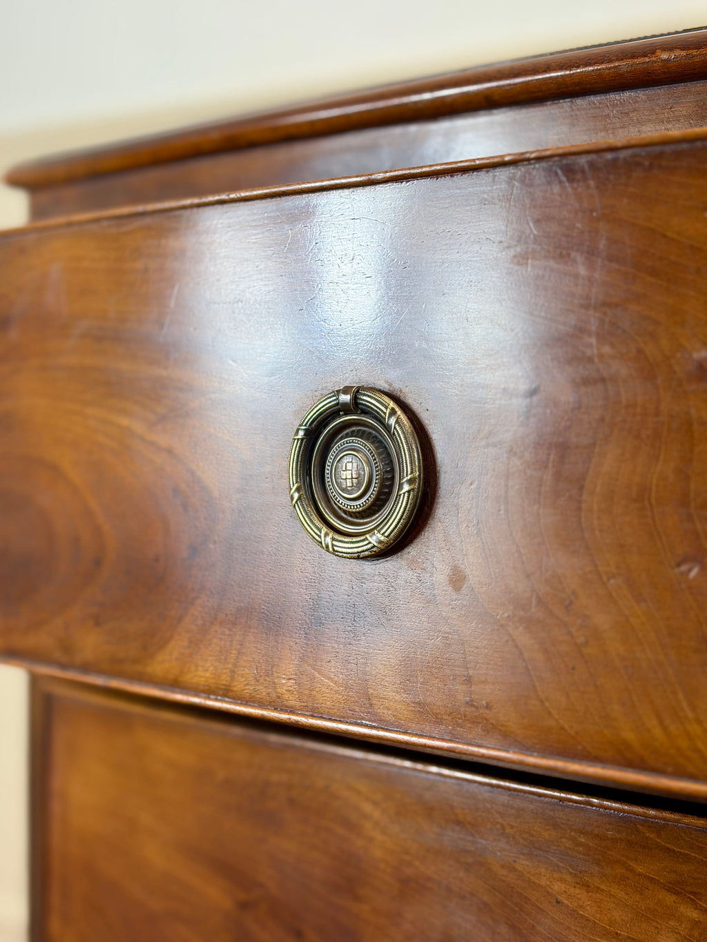 Close-up of a wooden drawer with a brass handle on a light-colored wall.
