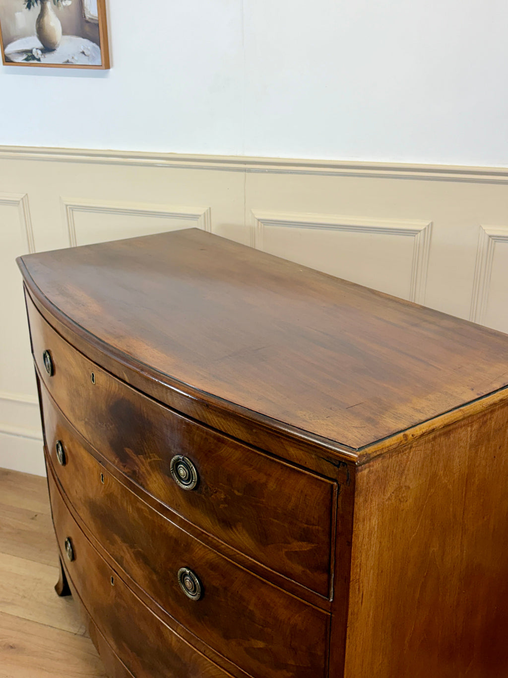 Wooden dresser with curved design against a white paneled wall.