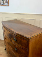 Wooden dresser with curved design against a white paneled wall.