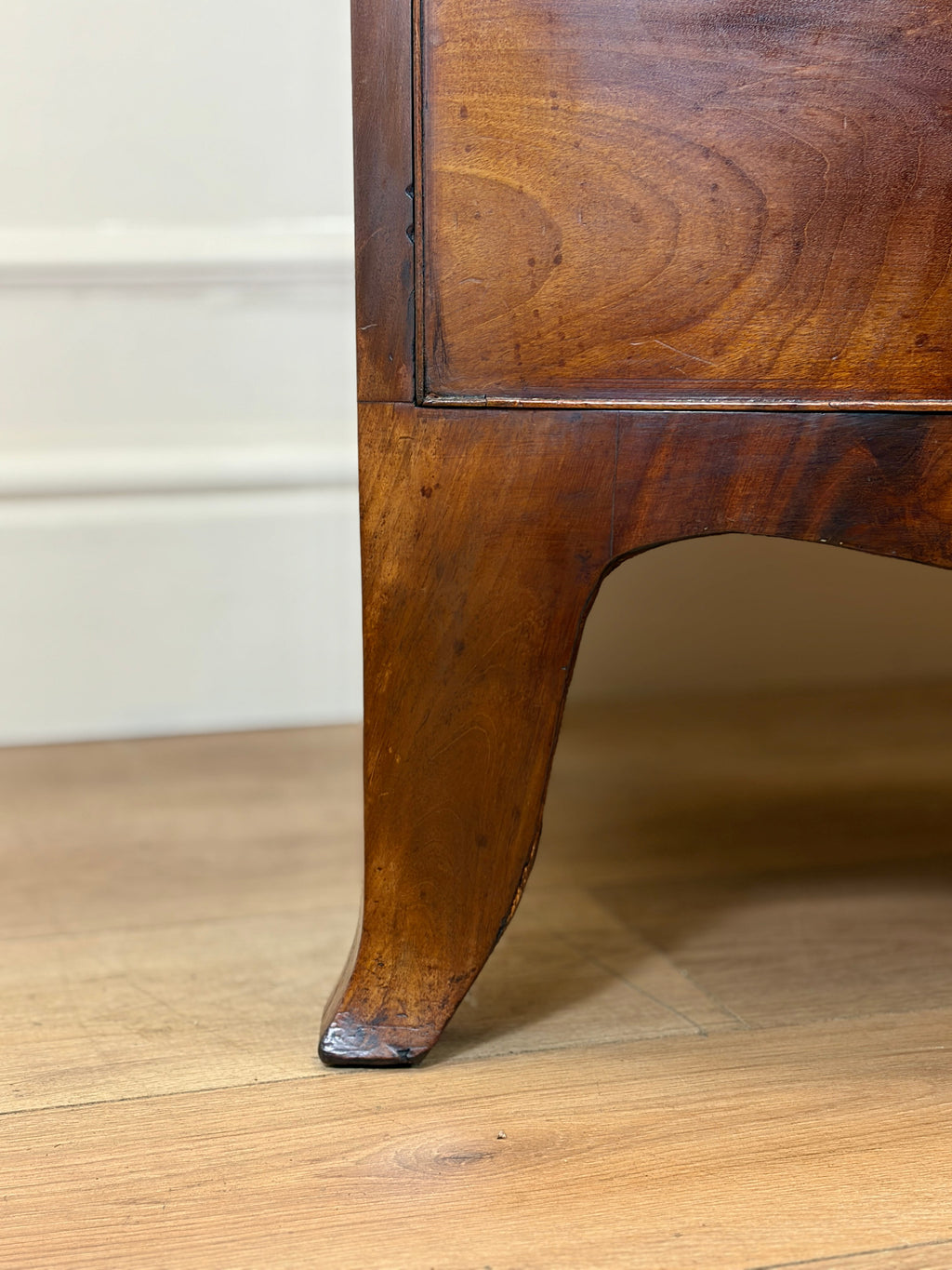 Close-up of a wooden furniture leg on a wooden floor with a white wall in the background