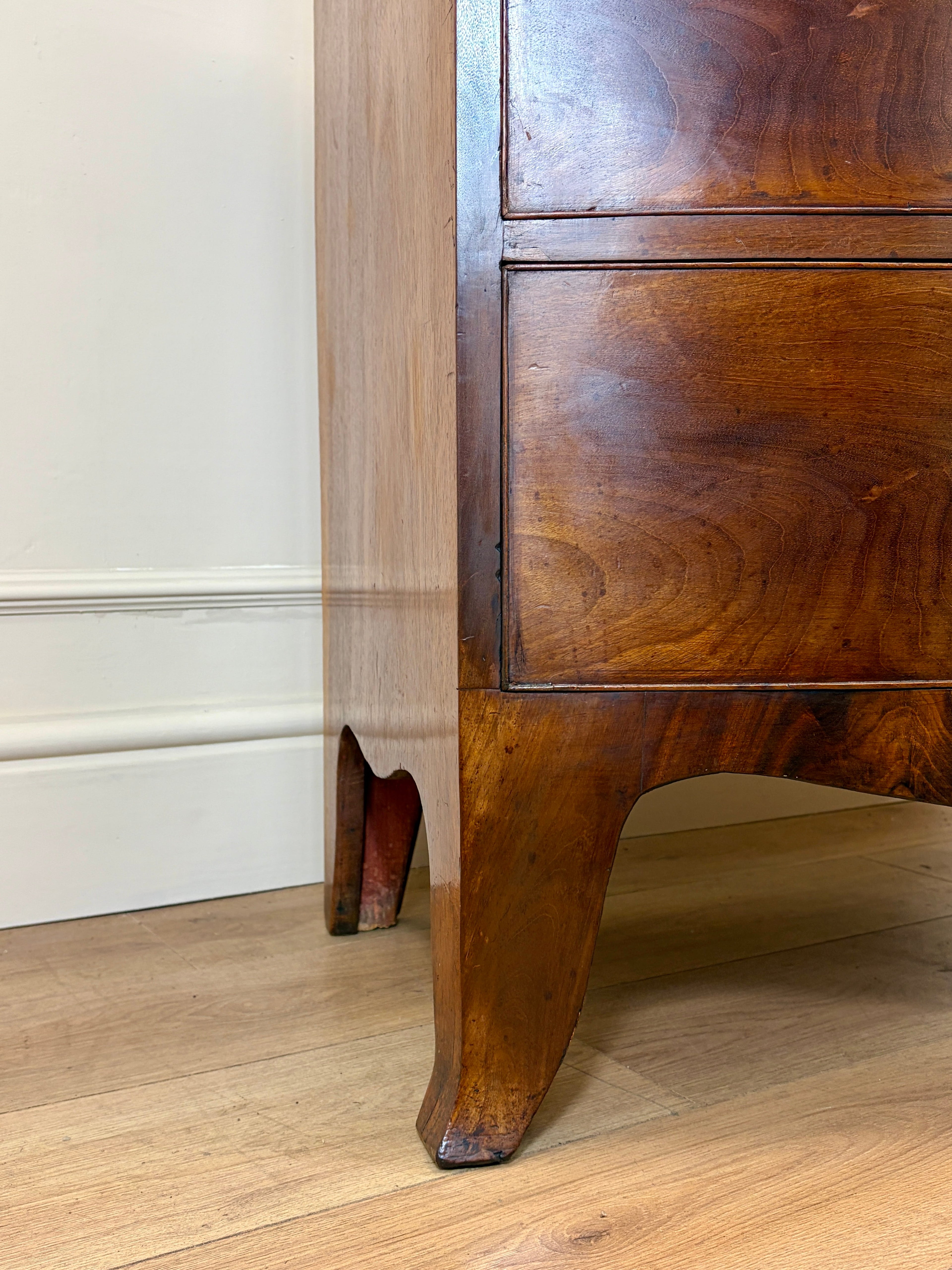 Wooden cabinet with a curved leg on a wooden floor against a white wall
