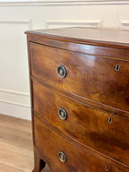 Wooden dresser with curved design and metal handles against a white wall.