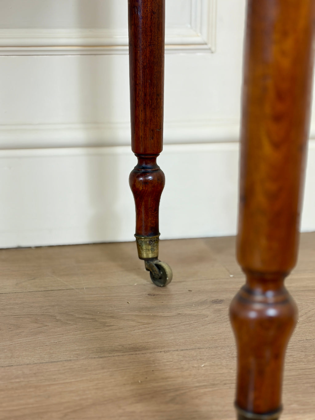 Close-up of a wooden leg with a caster wheel on a wooden floor.