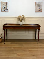 Wooden console table with decorative items against a wall with framed pictures.