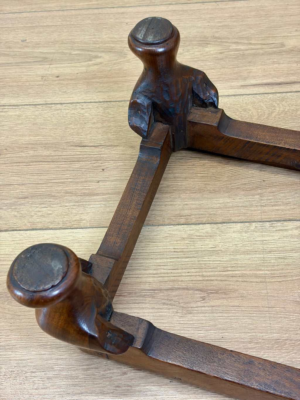 A close-up of a dark brown wooden carpenter's square or bevel square tool resting on a light wood plank surface.