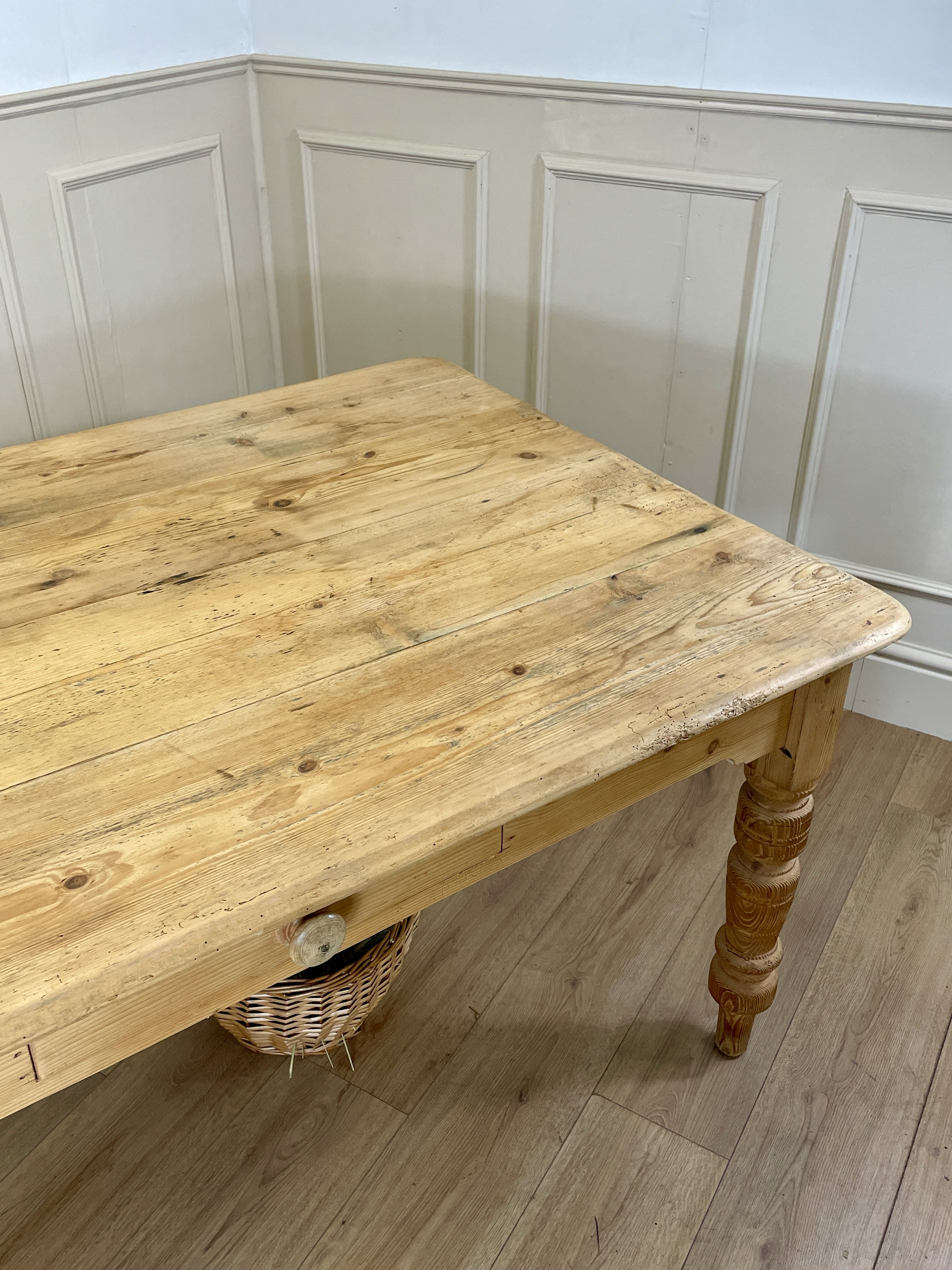 Wooden table with wicker basket underneath against a paneled wall.