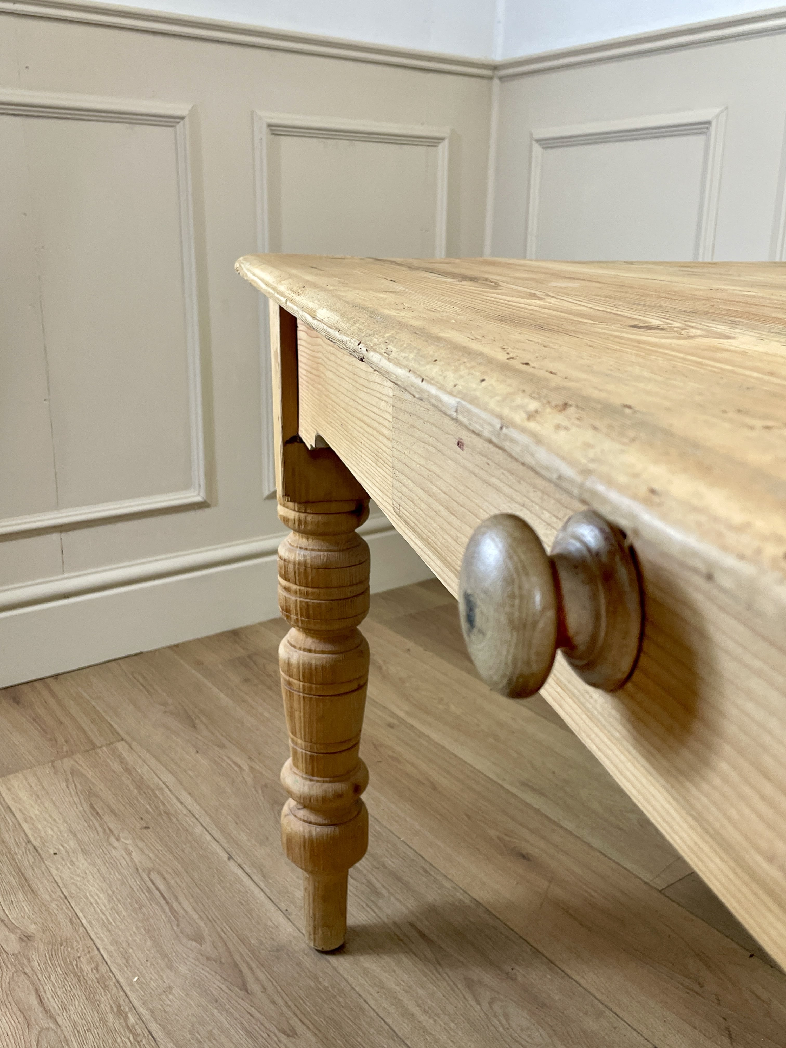 Wooden table with turned legs and decorative knobs against a paneled wall.