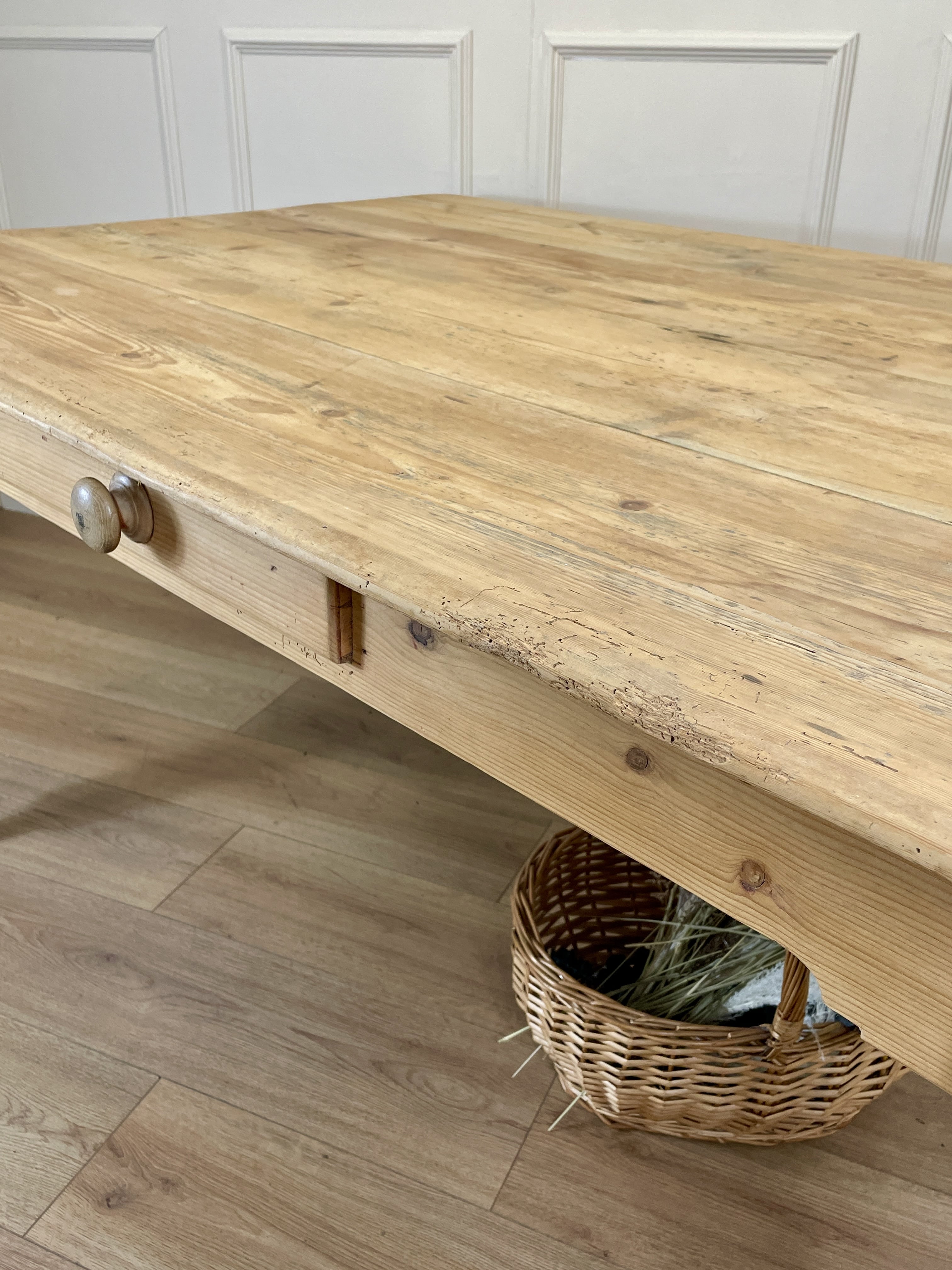Wooden table with a woven basket underneath on a wooden floor.