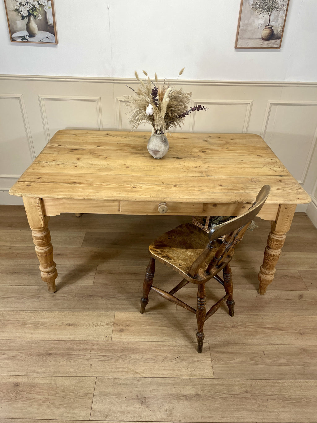 Wooden table with a vase of dried flowers and a matching chair on a wooden floor.
