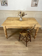 Wooden table with a vase of dried flowers and a matching chair on a wooden floor.