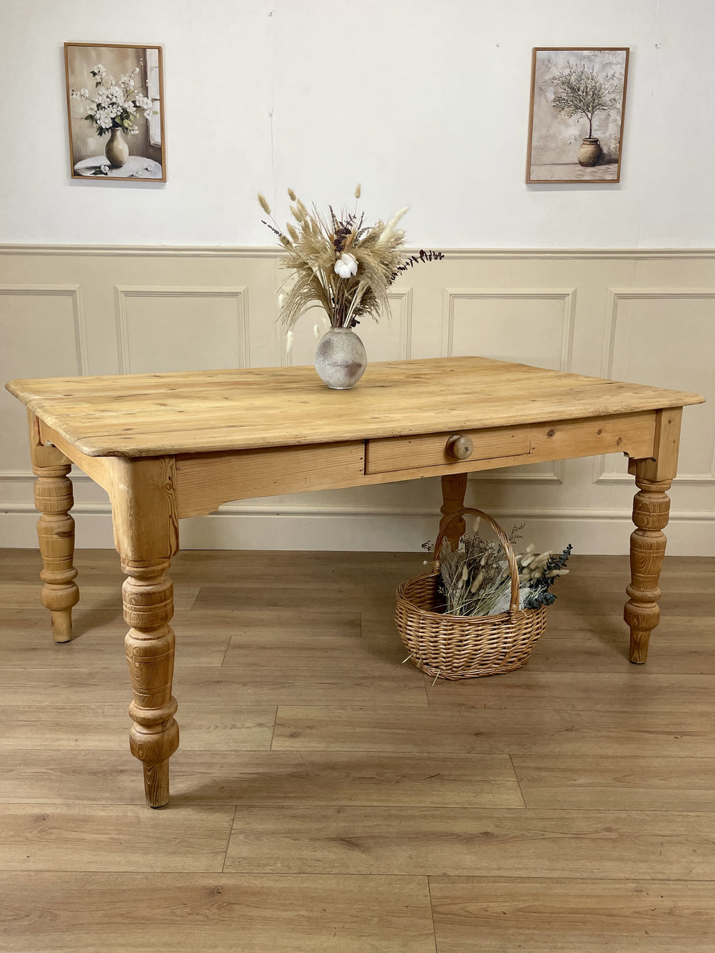 Wooden table with decorative items in a room with wainscoting and framed pictures.