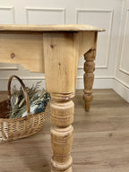 Wooden table with turned legs against a white paneled wall.