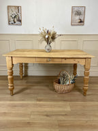 Wooden table with a vase and basket on a wooden floor, with two framed pictures on the wall.