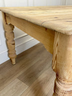 Wooden table with turned legs on a wooden floor against a white wall.