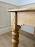 Close-up of a wooden table leg and top against a neutral wall.