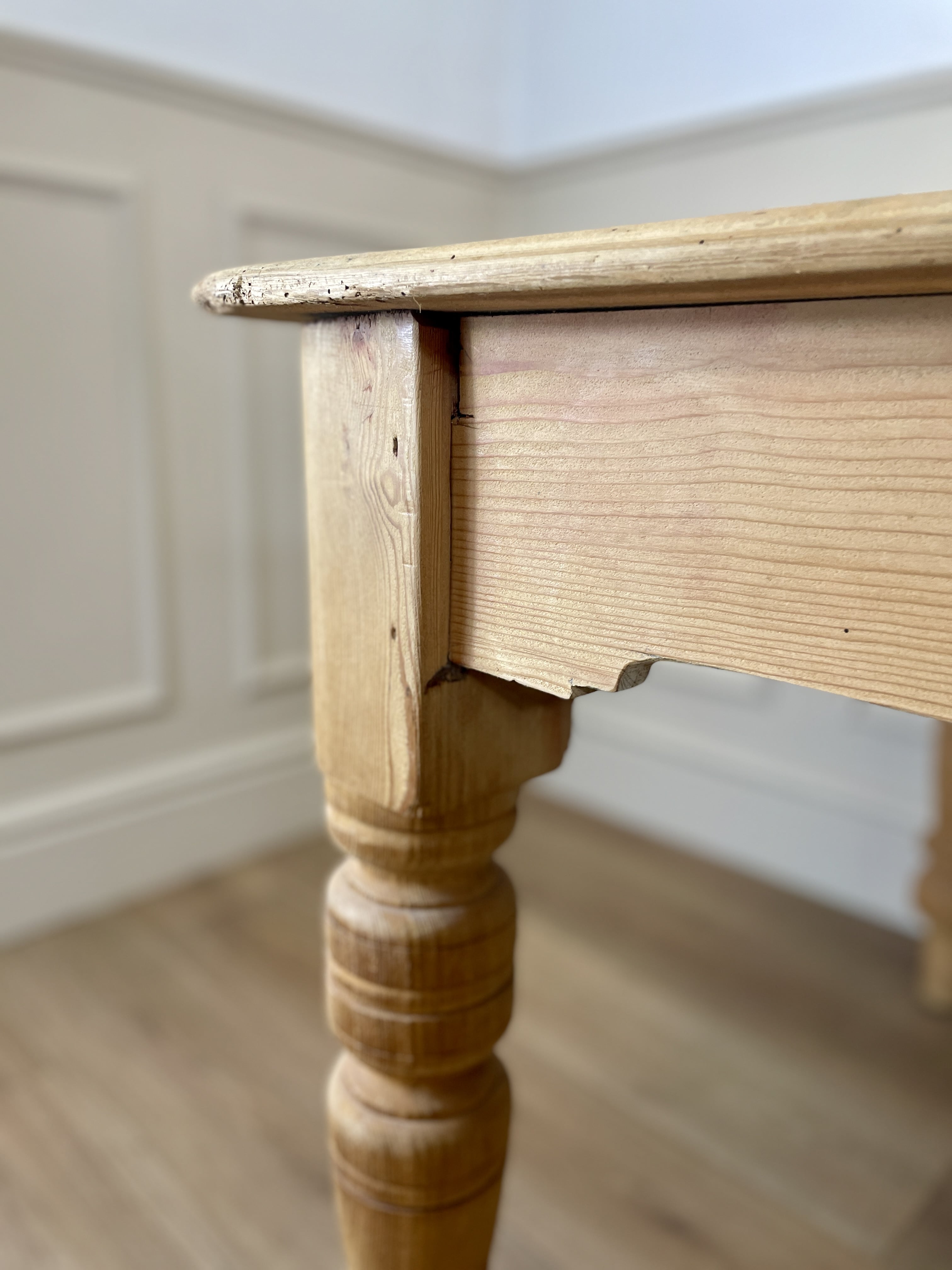 Close-up of a wooden table leg and top against a neutral wall.