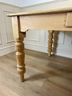 Wooden table with turned legs on a wooden floor against a white paneled wall.