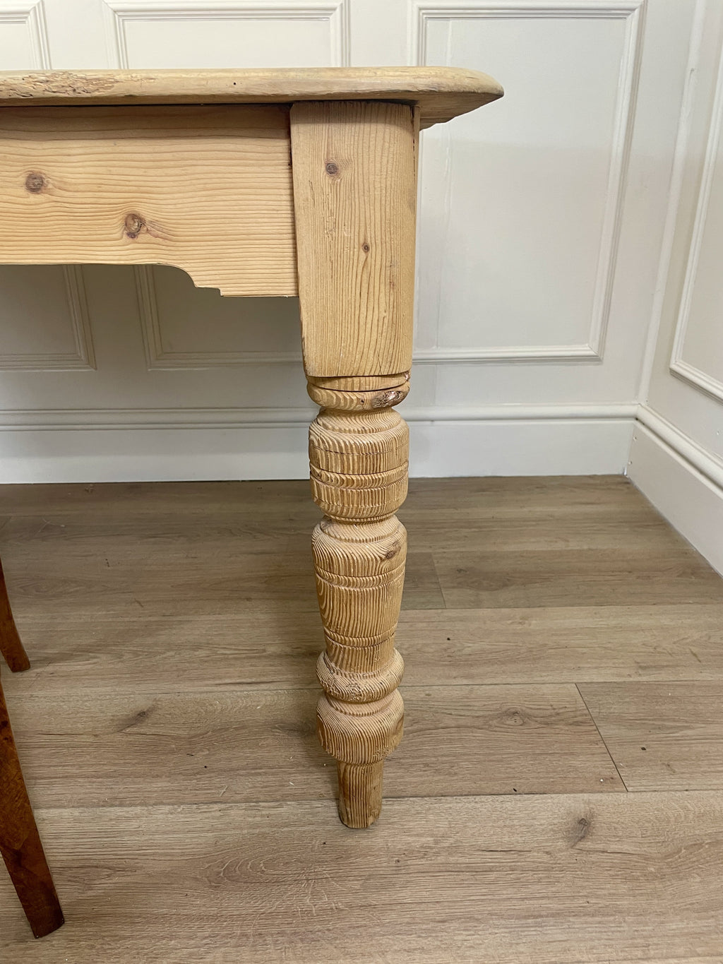Wooden table leg with a turned design on a wooden floor.