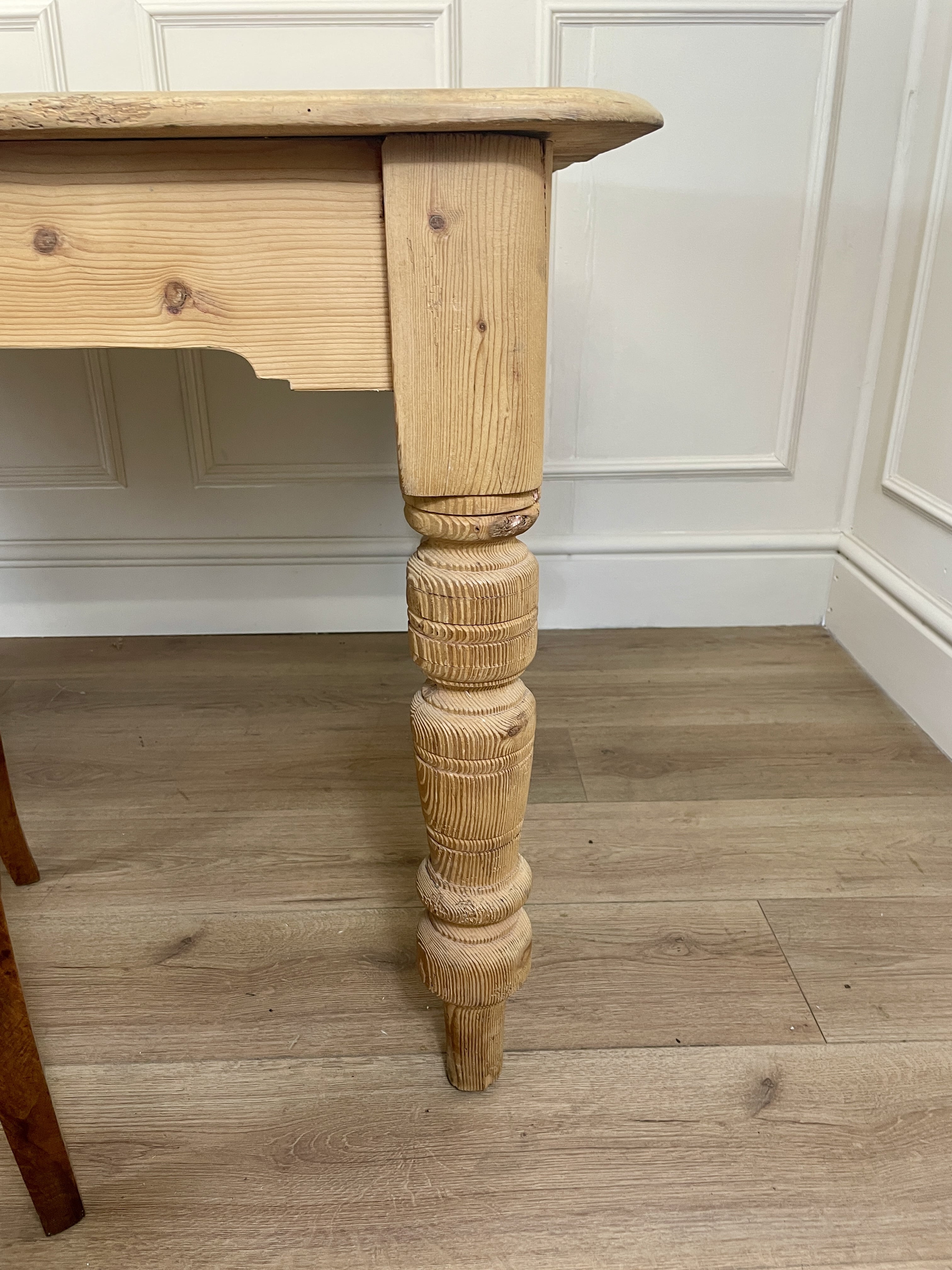 Wooden table leg with a turned design on a wooden floor.