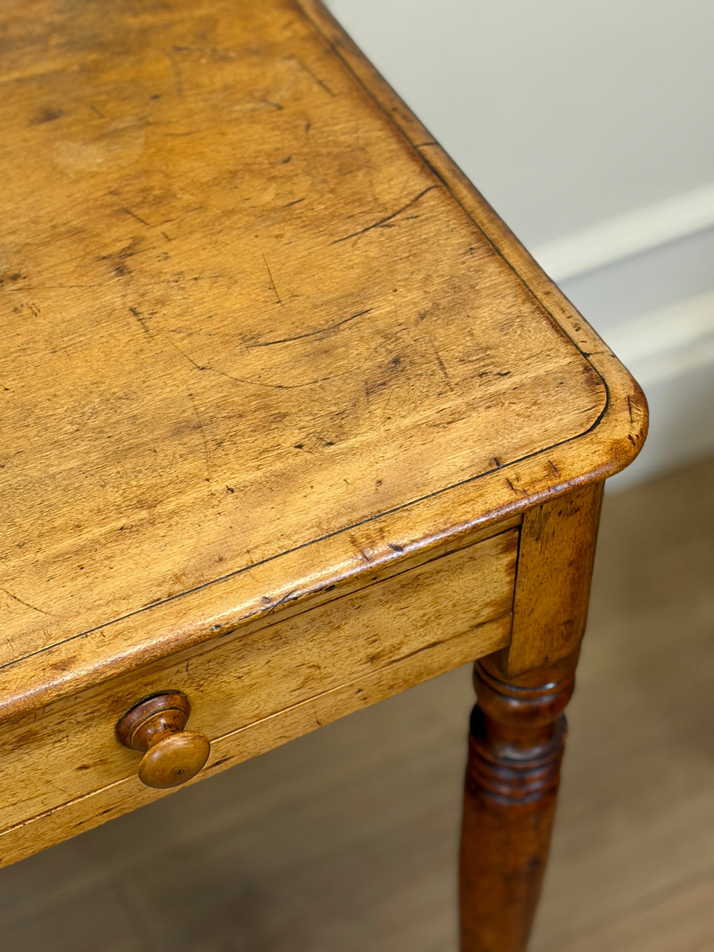 Close-up of a wooden table with a drawer and visible wear.