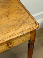 Close-up of a wooden table with a drawer and visible wear.
