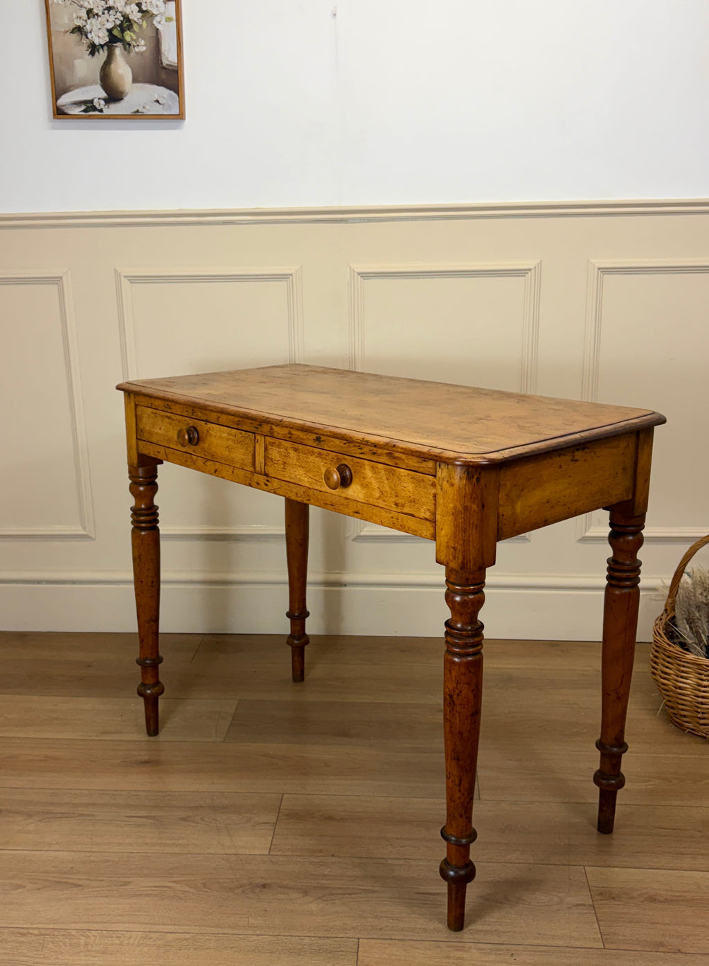 Wooden table with a single drawer against a white paneled wall.