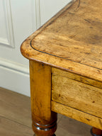 Close-up of a wooden table with visible wear and tear against a white wall.