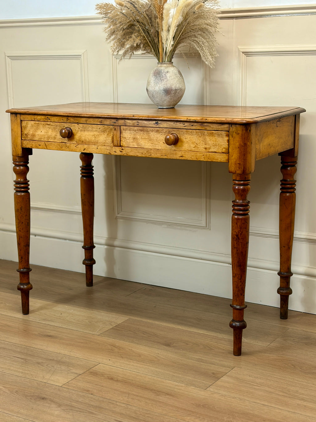 Wooden console table with two drawers against a white paneled wall.