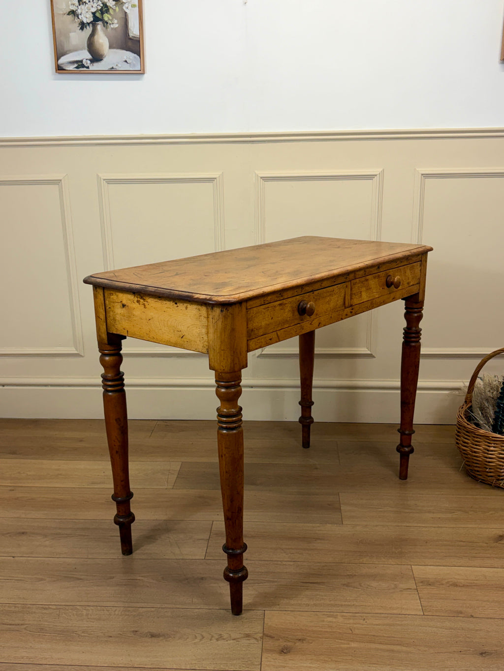 Wooden table with a single drawer on a wooden floor against a white paneled wall.