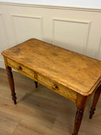 Vintage wooden desk with a single drawer against a white paneled wall.