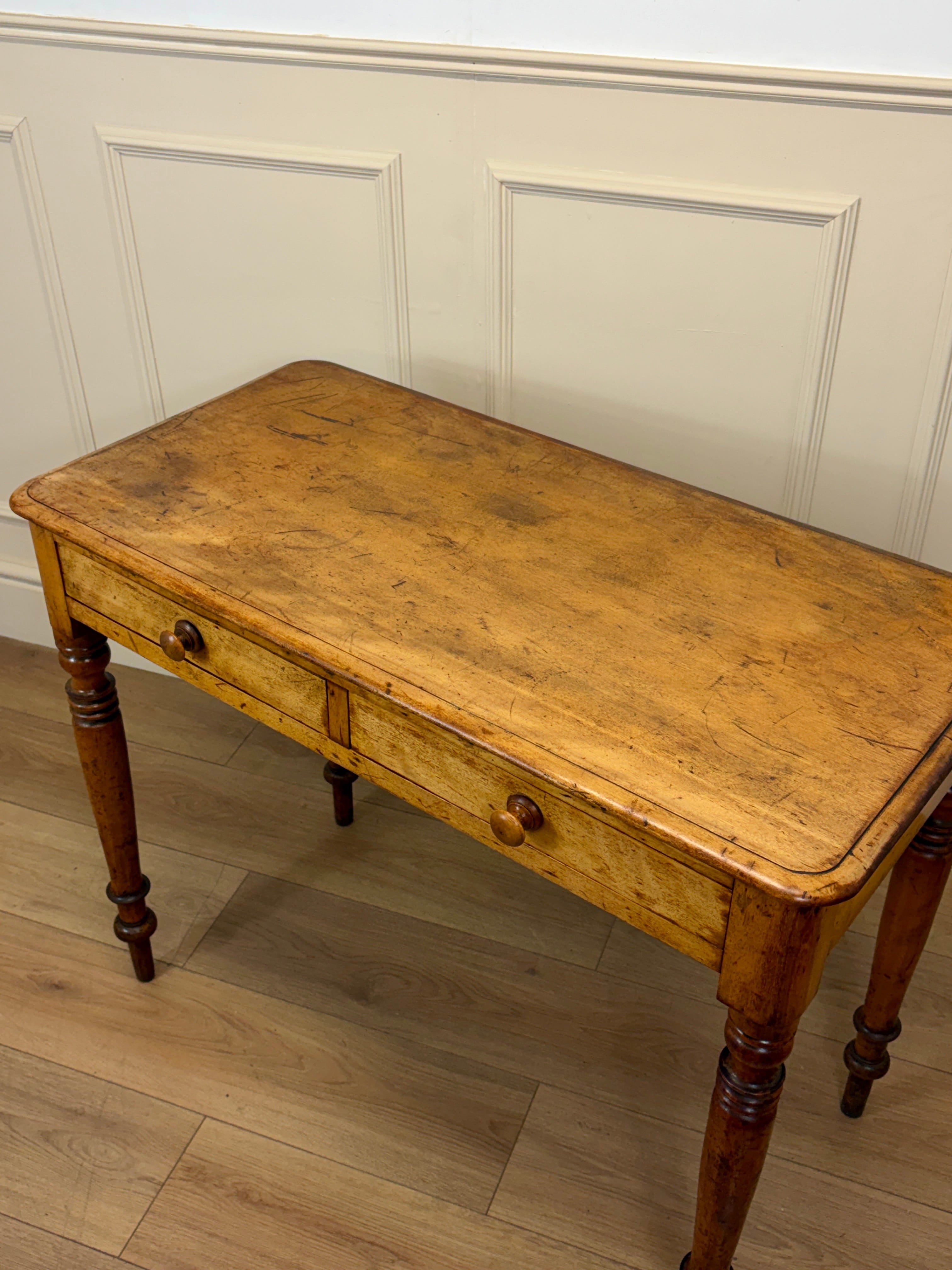 Vintage wooden desk with a single drawer against a white paneled wall.