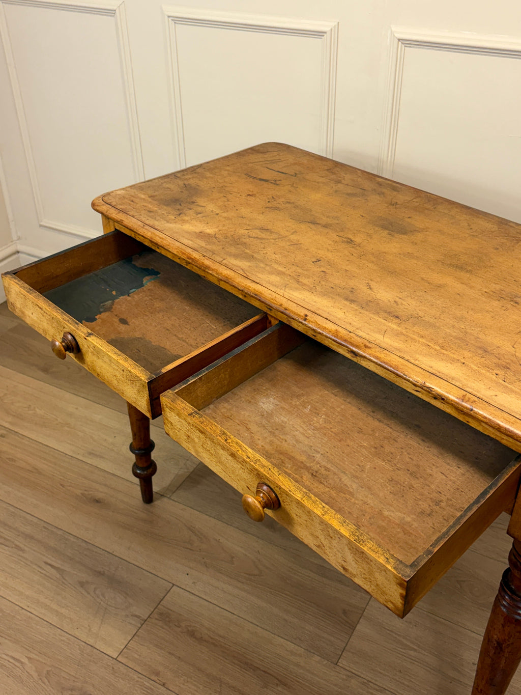 Wooden desk with two drawers in a room with white paneled walls.