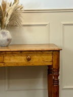 Wooden console table with a vase of dried plants against a paneled wall.
