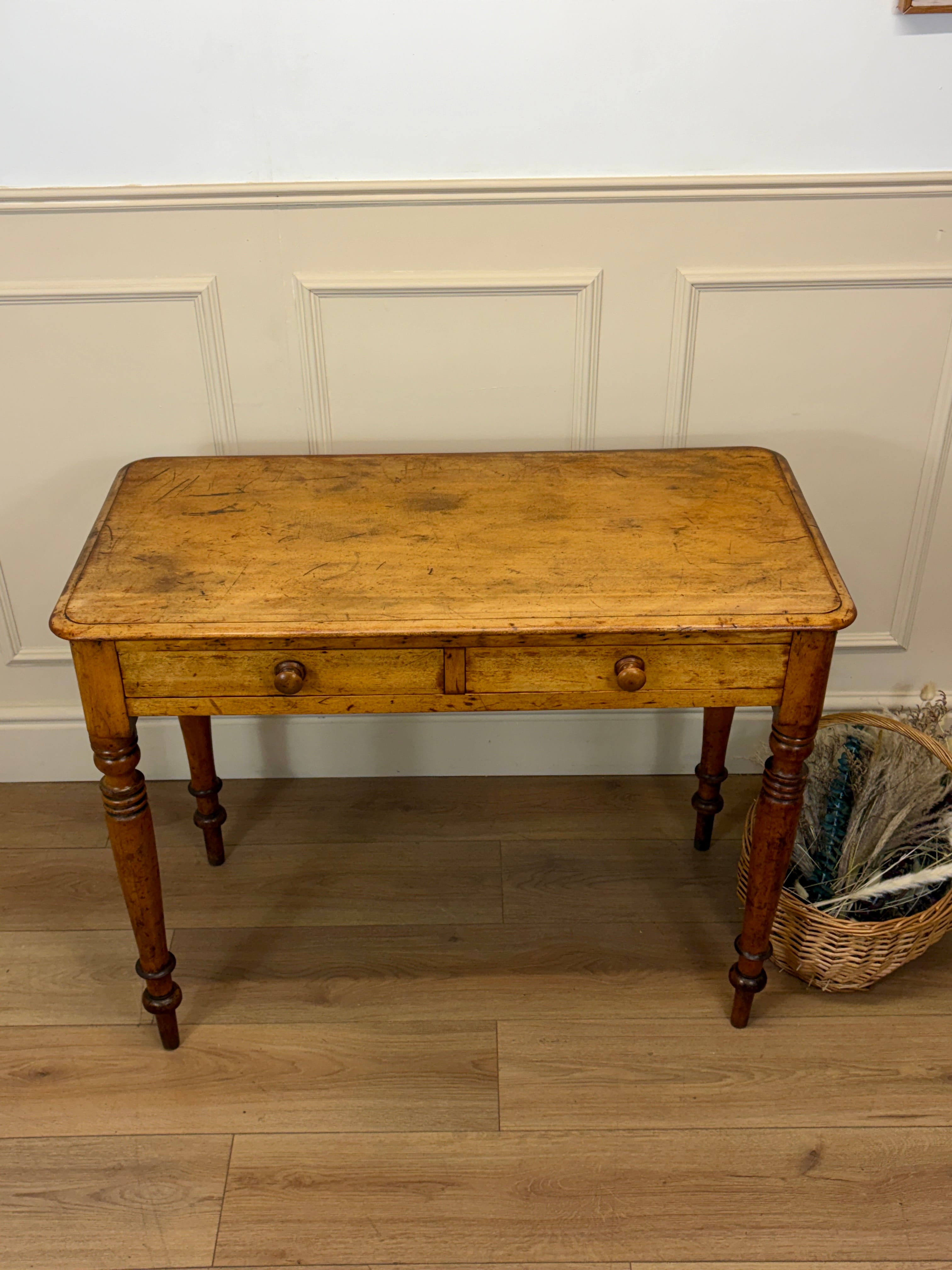 Wooden table with a single drawer against a white paneled wall.