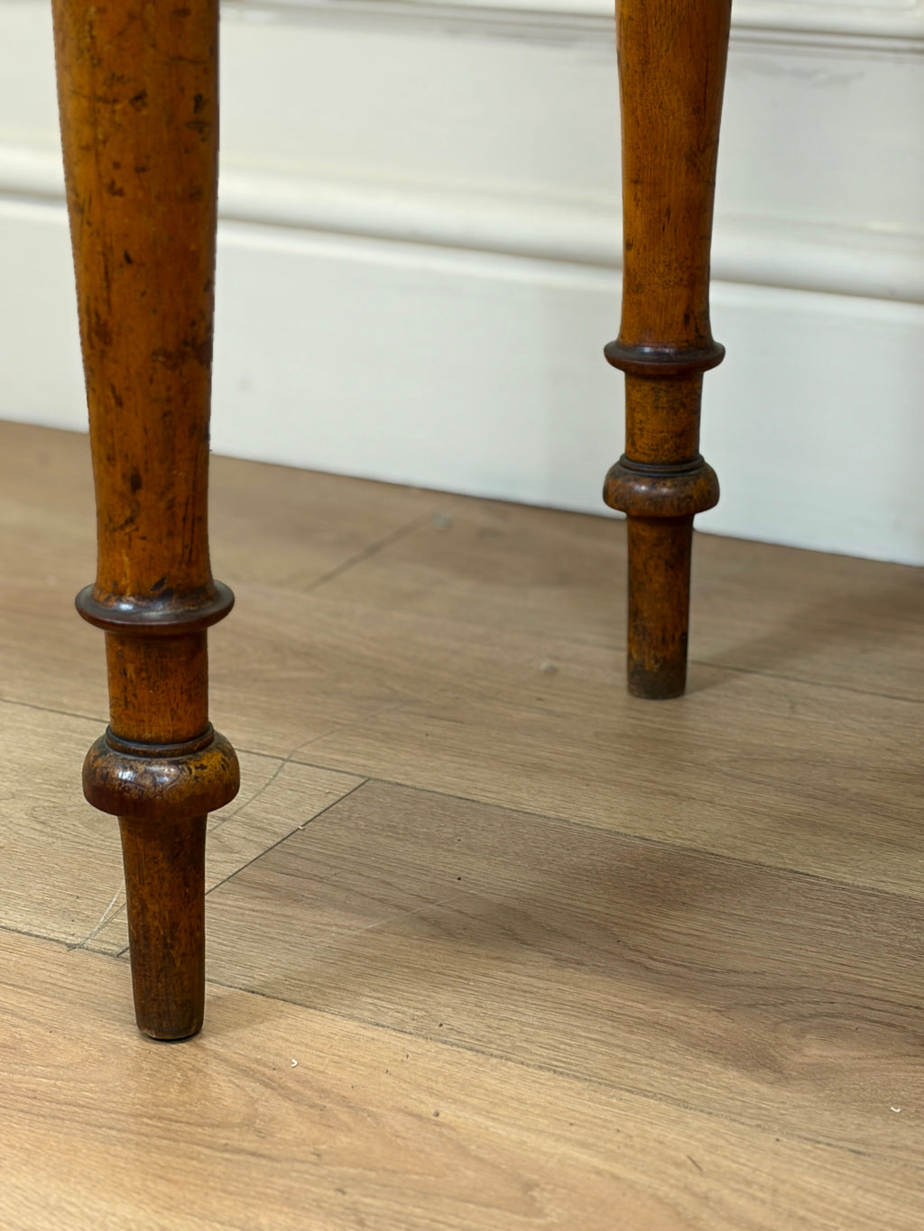 Close-up of wooden legs on a piece of furniture with a light wood floor and white wall background.