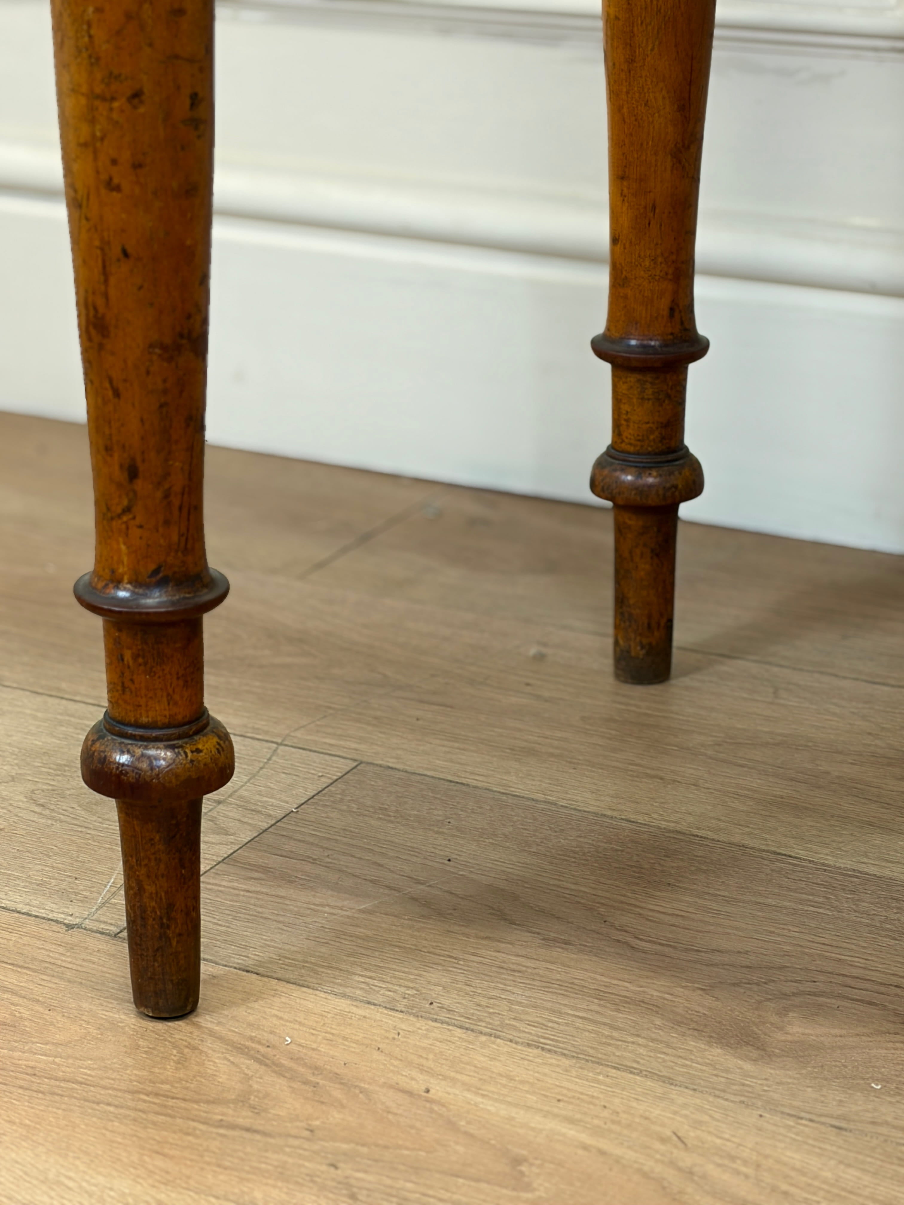 Close-up of wooden legs on a piece of furniture with a light wood floor and white wall background.