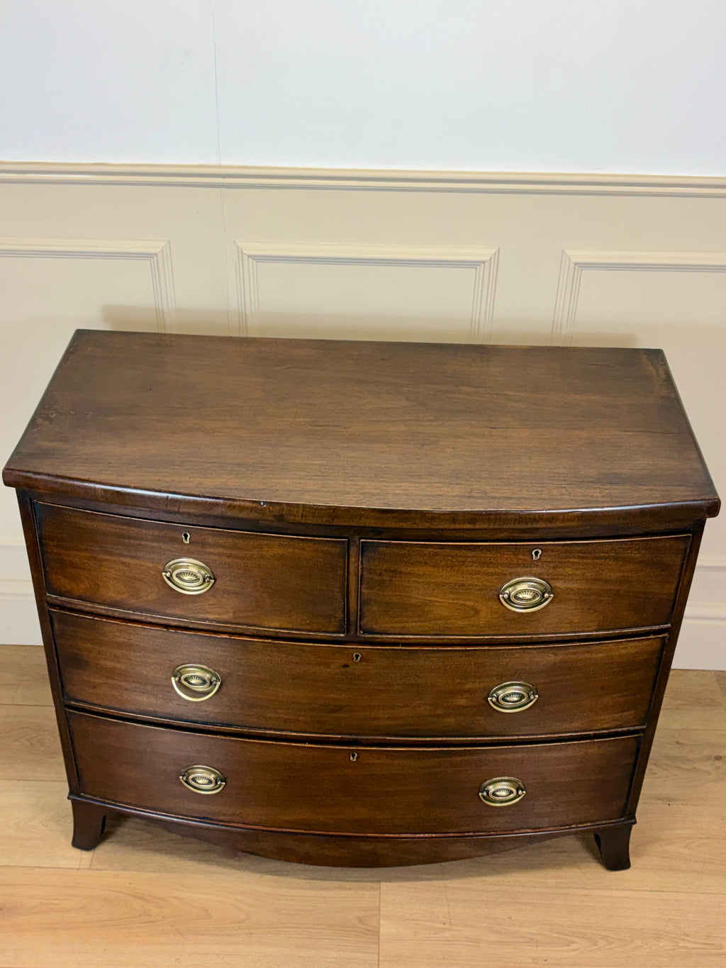 Wooden dresser with four drawers on a wooden floor against a white wall.