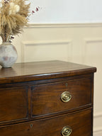 Wooden dresser with a vase of dried flowers on top against a beige wall.