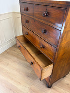 Wooden dresser with open drawer on a wooden floor against a white wall.