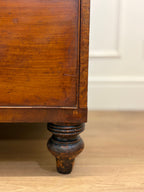Close-up of a wooden cabinet leg on a wooden floor with a white wall in the background