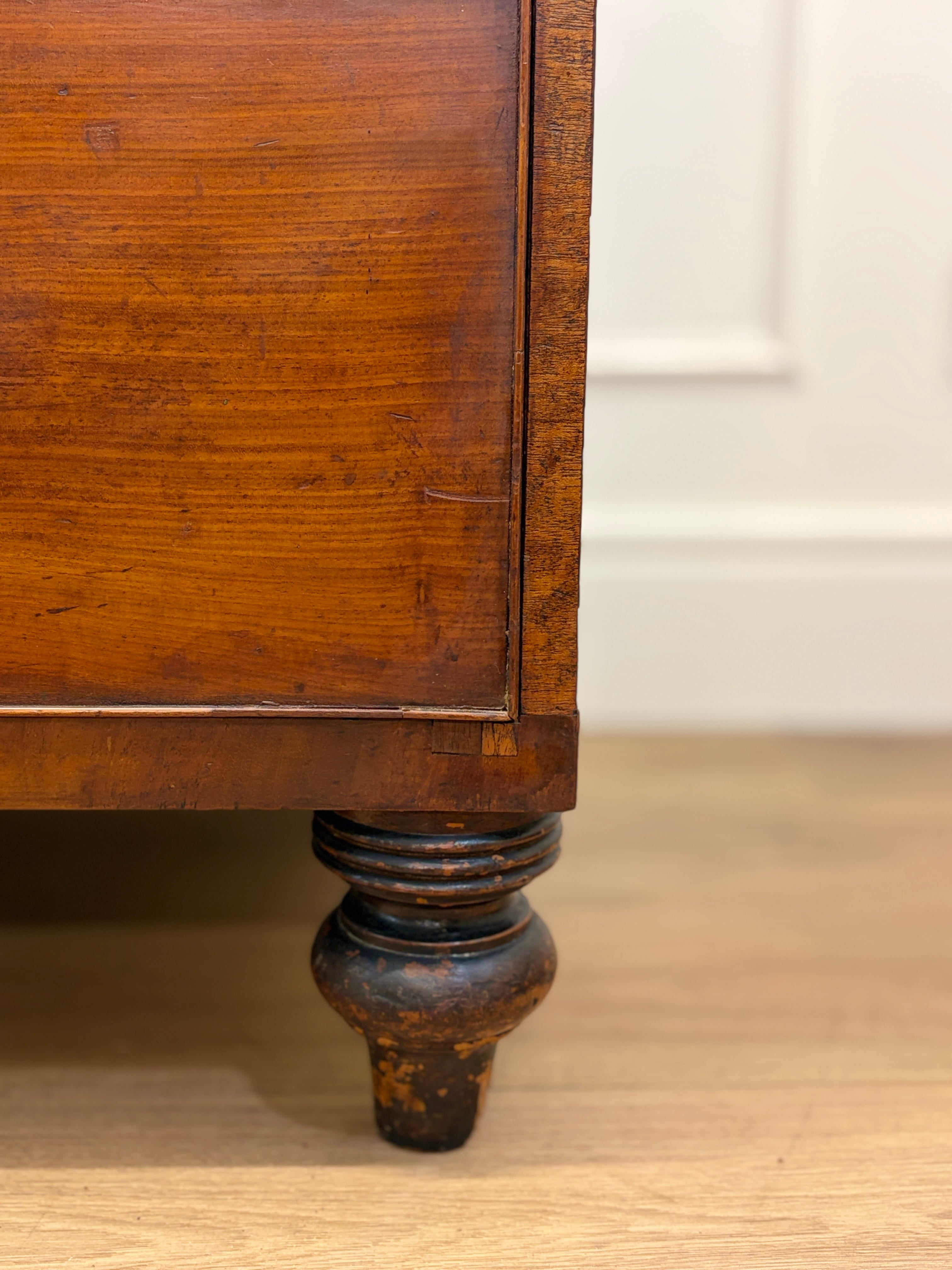 Close-up of a wooden cabinet leg on a wooden floor with a white wall in the background