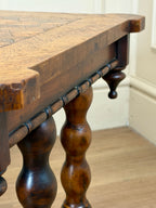 Close-up of a wooden table with turned legs in a room setting.