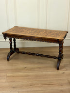 Wooden table with intricate legs on a wooden floor against a white paneled wall.